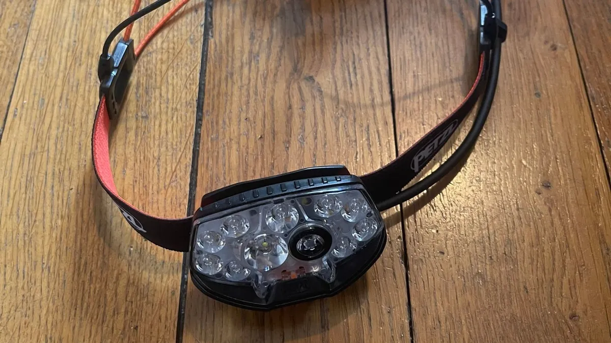 La frontale Petzl Nao RL posée sur un parquet, vue de face, avec ses LED et son bandeau rouge