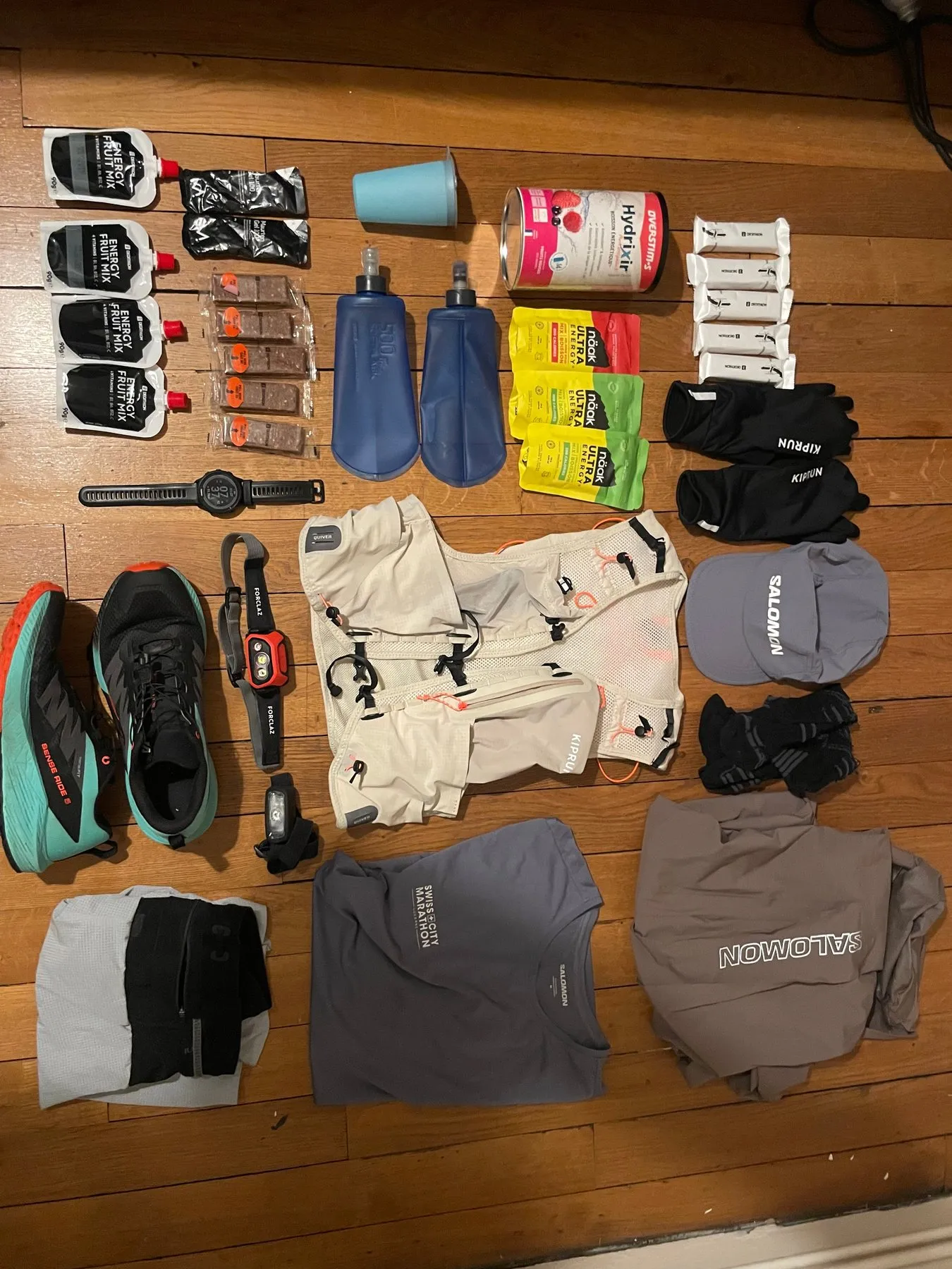 Le matériel de Nicolas pour la SaintéLyon étalé au sol : gels, flasques, frontale, sac, chaussures, gants, casquette et vêtements